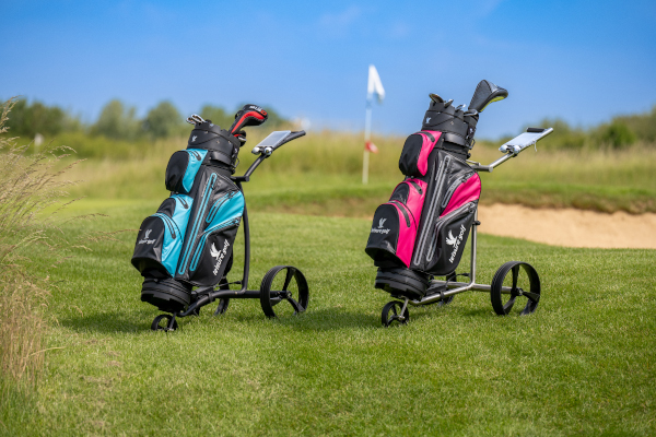 Zwei Elektor-Golf-Trolleys in blau-schwarz und rot-schwarzstehen auf einem Golfplatz, im Hintergrund ist eine Sandkuhle