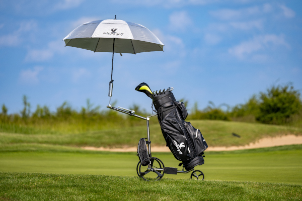 Grauer Golfschirm an einem Elektro-Golf-Trolley stehend auf einer grünen Golfwiese